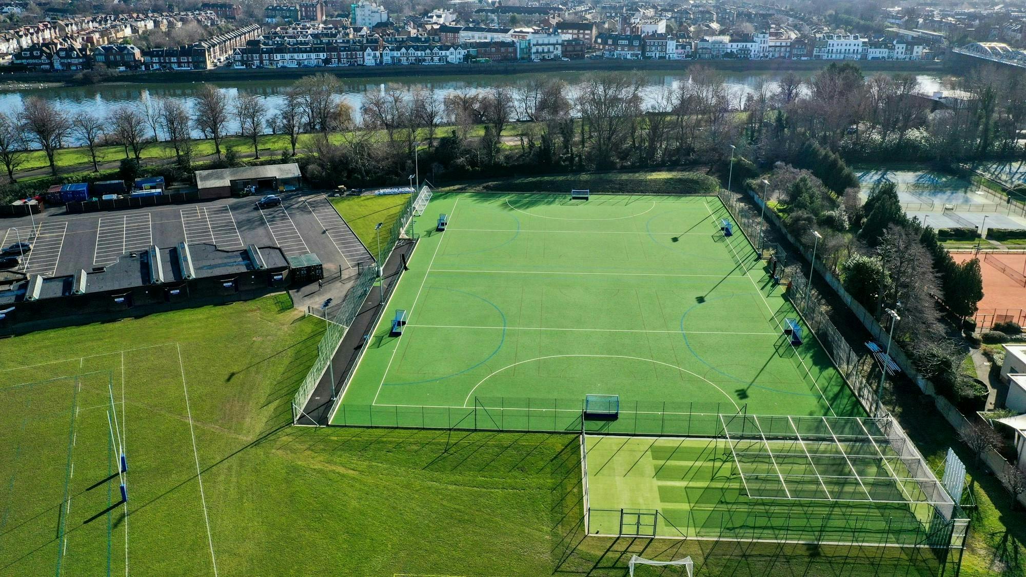 King's House Sports Ground in Chiswick as seen from above with a 3G ptich front and centre and the Rive Thames in the background behind a row of trees