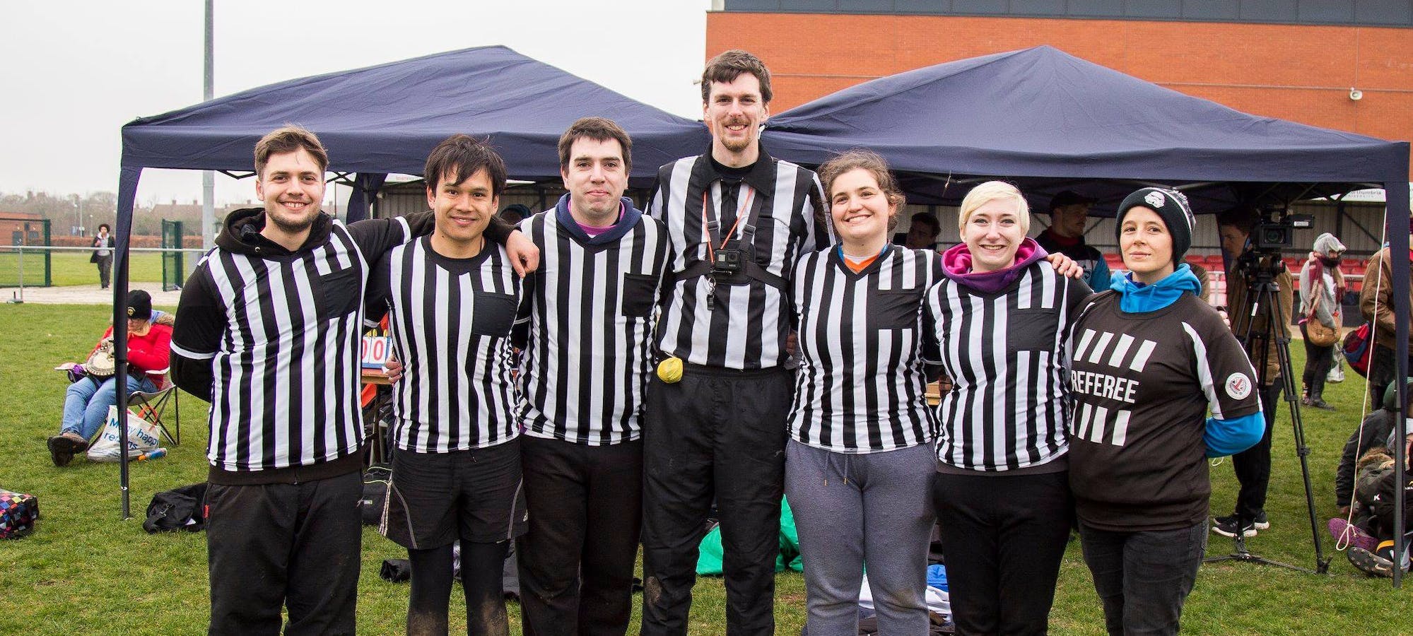 A ref team poses together before a match, all wearing their striped ref shirts